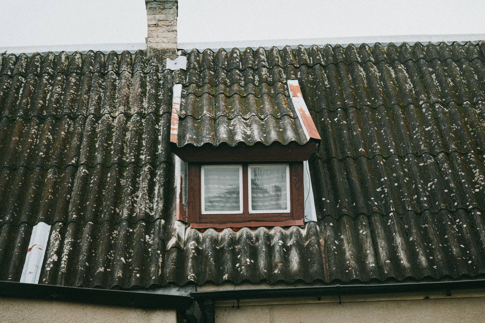 Bemoostes altes Wellplattendach mit kleiner Gaube an einem Wohnhaus als Symbolbild für verborgene Mängel und Schadstoffrisiken beim Hauskauf